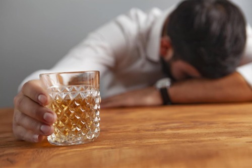 a man with his head down holds a drink and wonders when does binge drinking become a problem