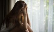 girl sits by window holding her head in her hands and crying as she's dealing with anxiety