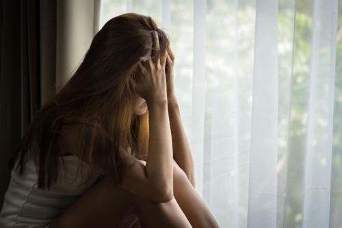 girl sits by window holding her head in her hands and crying as she's dealing with anxiety