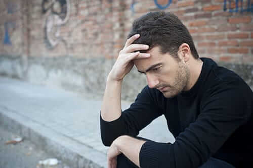Man sitting on curb with hand to forehead wondering if a dual diagnosis treatment program can help him