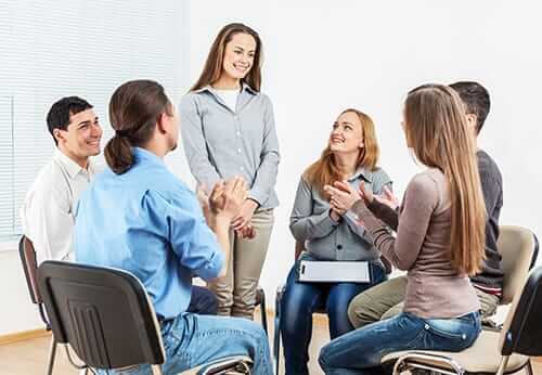 A young woman standing in group therapy for addiction session