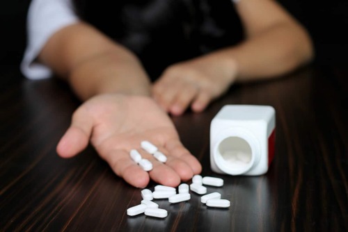 white pill bottle with white pills spilled on table and person holding some pills showing the long term side effects of xanax