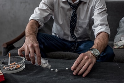 businessman pours pills on table next to an ashtray full of cigarettes and realizes he needs an mdma detox program