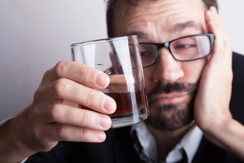 a man staring at his glass not thinking about the signs of alcoholism