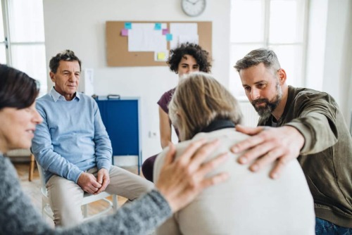 Men and women sitting in a circle during group therapy, supporting each other. group therapy session