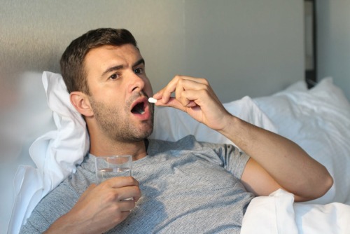 man in bed taking a pill wondering what is the opioid crisis