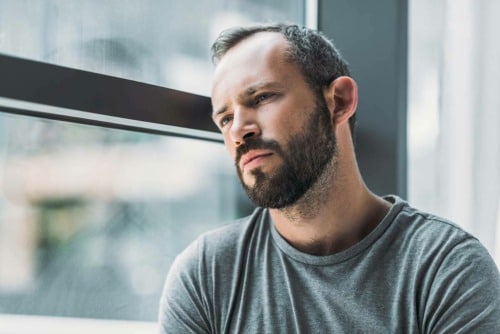 pensive man next to a window wondering what makes drugs addictive and are all drugs addictive