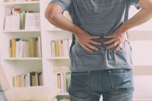 Man, struggling with back pain management without drugs, holding his back