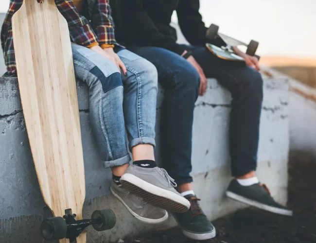 two young adults sitting on a concret wall with their skate boards.