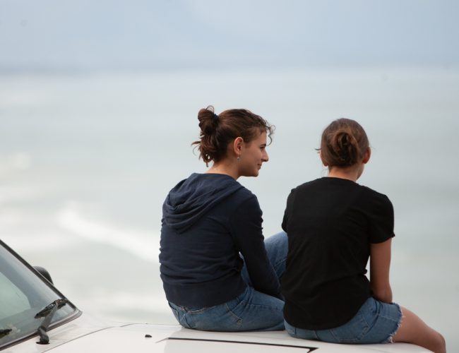 two women sitting on the hood of a car speaking about addiction aftercare program in houston