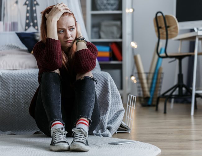 Worried, young girl holding her head and looking away in her bedroom