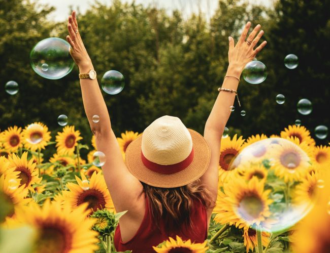 Woman sitting outside with her hands up and celebration in a bed of flowers
