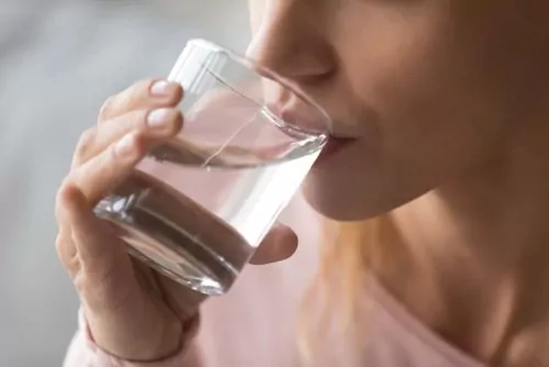 Woman drinking a glass of water, trying to replace unhealthy habits with healthy ones