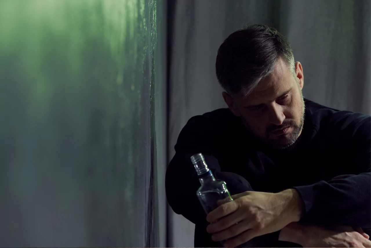 man sitting on the ground holding a bottle of alcohol struggling with red nose alcohol symptoms