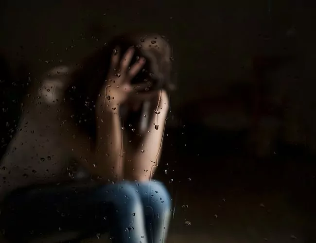 woman bent over holding her head in a dark room needing addiction aftercare program in houston
