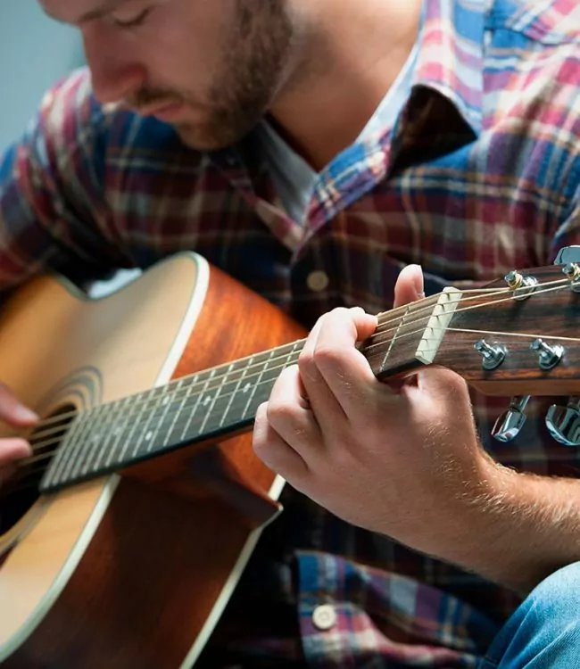 man sitting on the couch playing with his guitar during music therapy